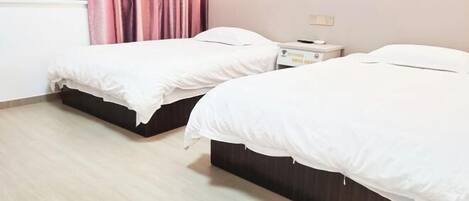 A hotel room with two single beds, a bedside table with a lamp, and a window with curtains.
