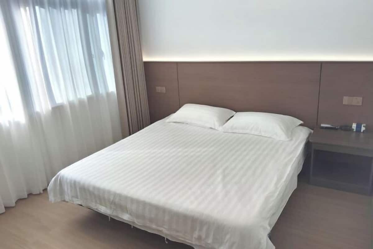 Una habitación de hotel con cama, mesita de noche y ventana con cortinas.