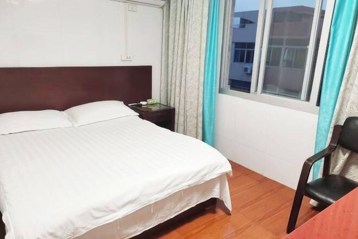 Una habitación de hotel con cama, mesita de noche, una silla y una ventana con cortinas.