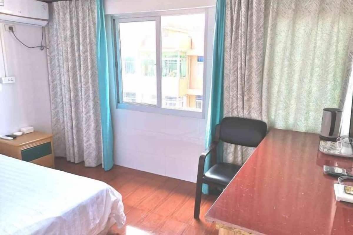 Una habitación de hotel con cama, escritorio, silla, ventana y cortinas.