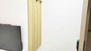 A room with a flat-screen TV mounted on the wall, a wooden panel with black hooks, and a partially visible door. - Zhulian Hostel (Wenzhou)