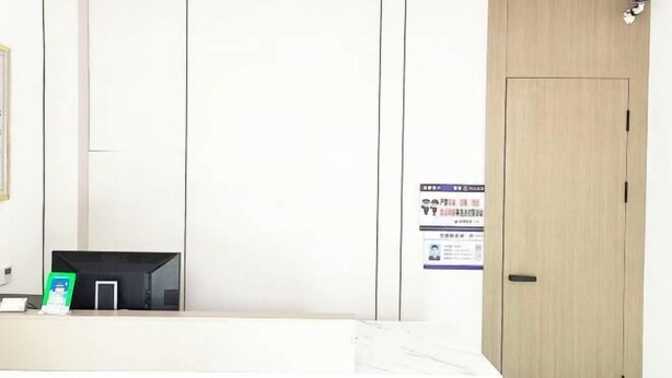 A hotel room with a marble floor, a wooden door, a reception desk with a green sign, and a wall-mounted poster. - Zhulian Hostel (Wenzhou)