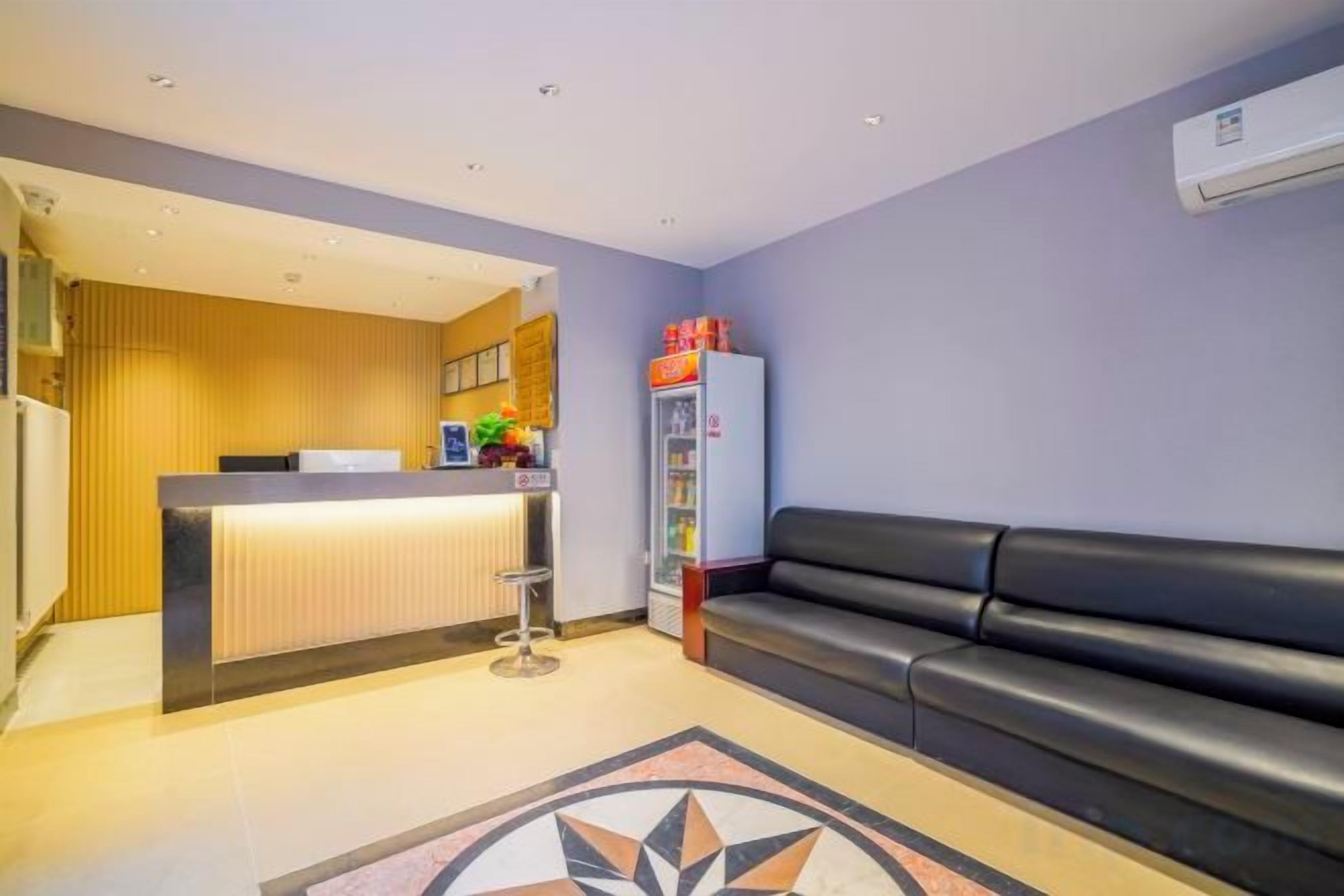 Un área de recepción con mostrador, refrigerador, sofá negro y alfombra estampada.