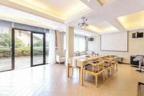 A modern hotel room with a large sliding glass door, a dining area with a wooden table and chairs, a flat-screen TV, and a projector. - Banmeiju GINLAN JIA Vacation Apartment (Jiande)