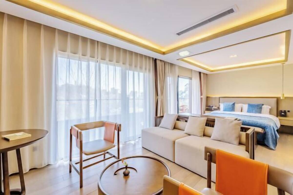 A hotel room with a sofa, a dining table, a round coffee table, and a bed with a blue bedspread.