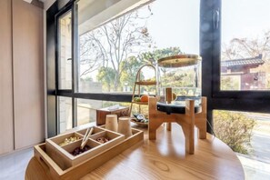 A room with a wooden table, a window with a view of trees and a building, and a traditional Japanese tea set.