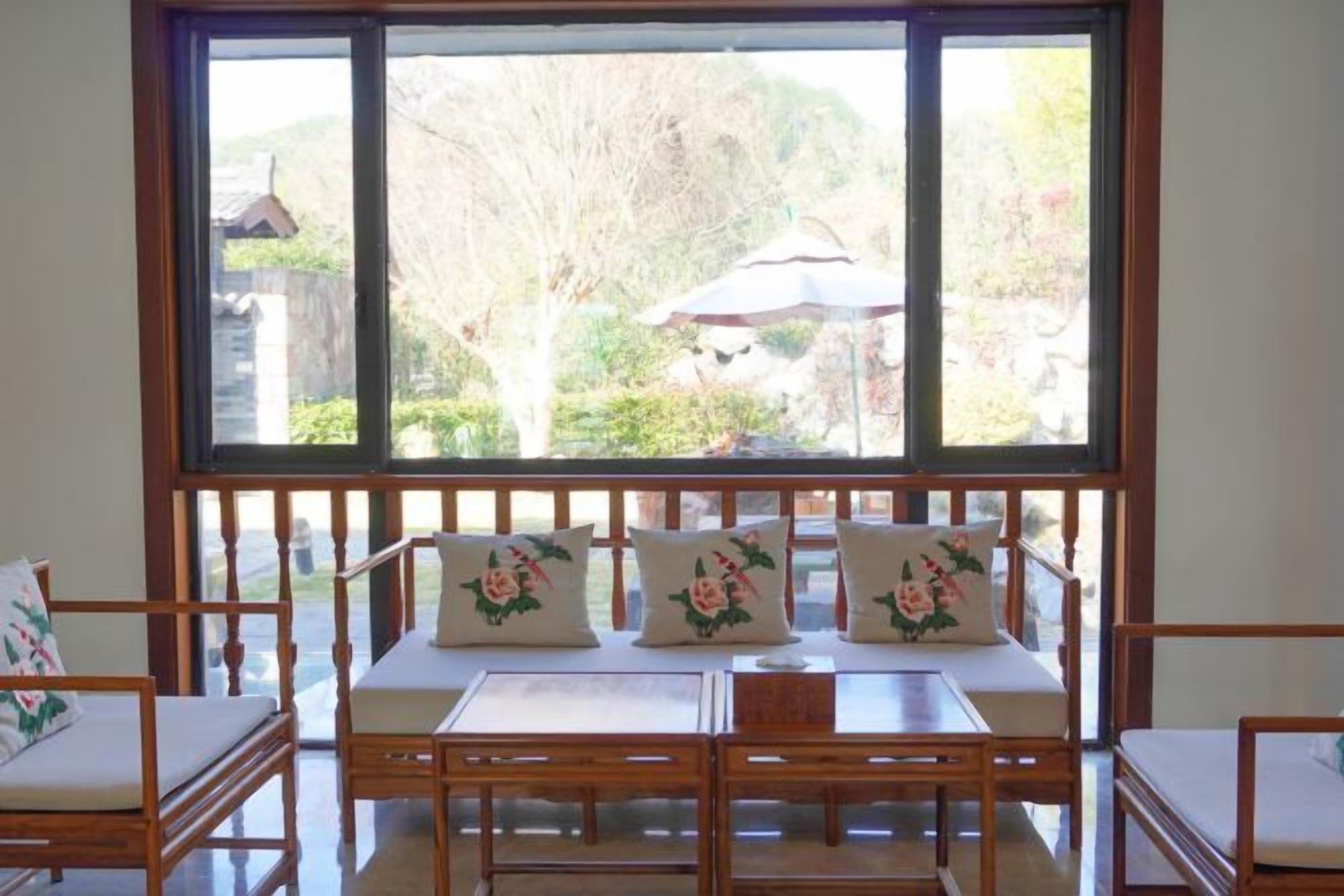Una habitación con un ventanal grande, un banco de madera con cojines florales y una mesa con sillas.