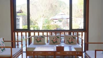 Una habitación con un ventanal grande, un banco de madera con cojines florales y una mesa con sillas.