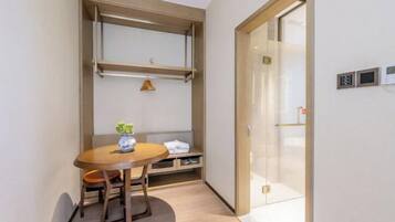 A compact room with a wooden table, a bench, and a small potted plant. There is a sliding door with a glass panel and a wall-mounted control panel.
