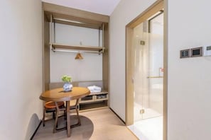 Ein kleines Zimmer mit einem Holztisch, einer Bank und einem kleinen Topfpflanzen. Eine Schiebetür mit Glasfenster und ein fest montiertes Bedienfeld.