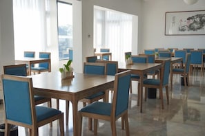 Un comedor con varias mesas y sillas, ventanas amplias y una obra de arte enmarcada en la pared.