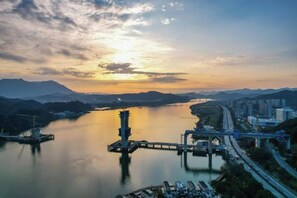Un río con un puente, un muelle y un paisaje urbano con edificios y montañas al fondo.