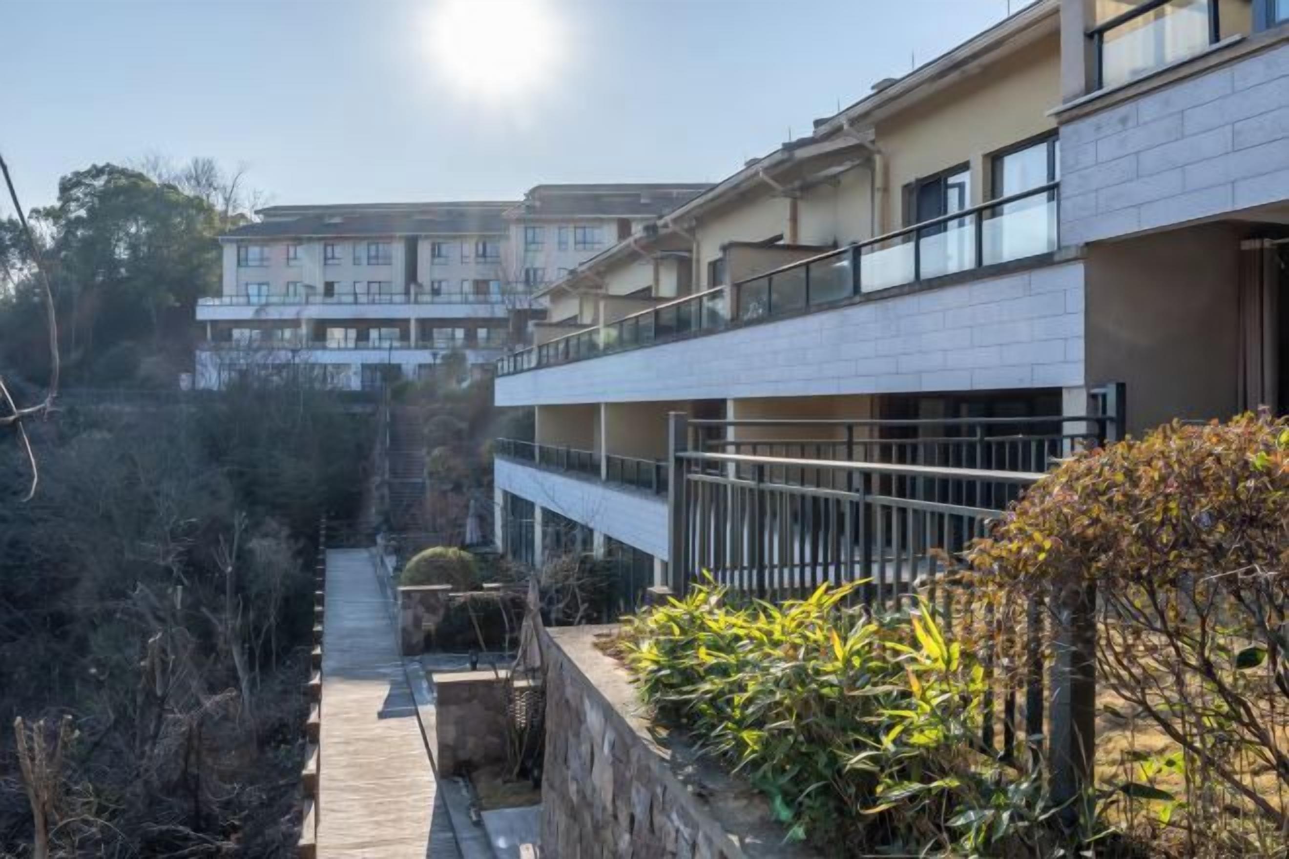 A residential building with a balcony, a pathway, and surrounding vegetation.