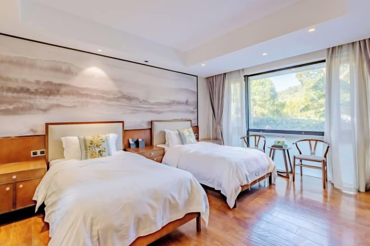A hotel room with two beds, a large window, and a wooden floor.