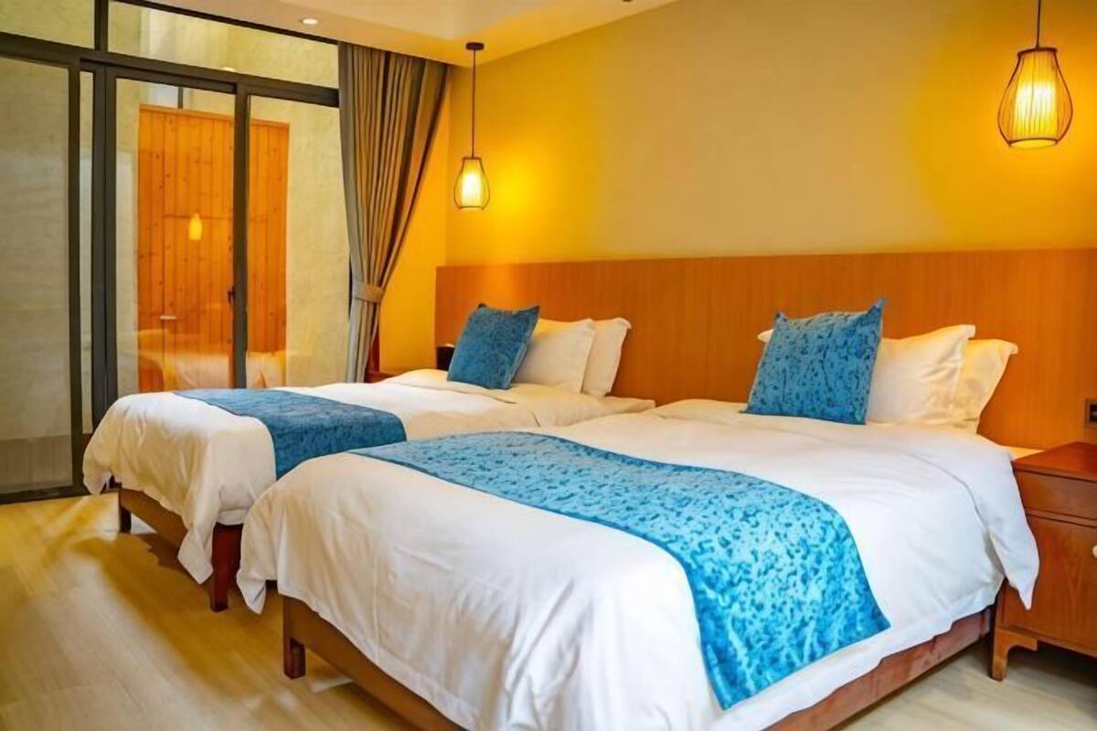 A hotel room with two beds, a wooden headboard, a nightstand, and a large window with curtains.