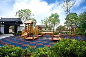 Un parque infantil con un tobogán de madera y estructuras de escalada, rodeado de un suelo a cuadros y follaje.