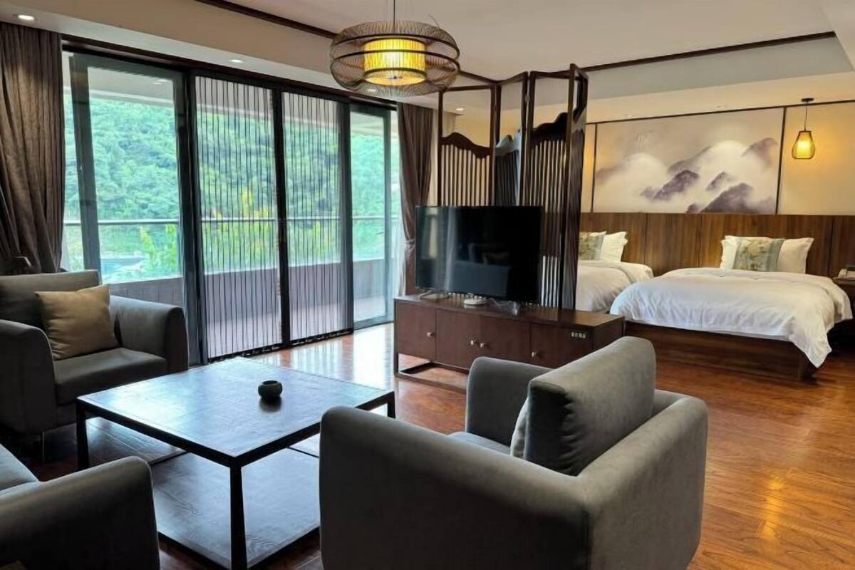 A modern hotel room with a large bed, a television on a wooden cabinet, a sofa, and a dining table.