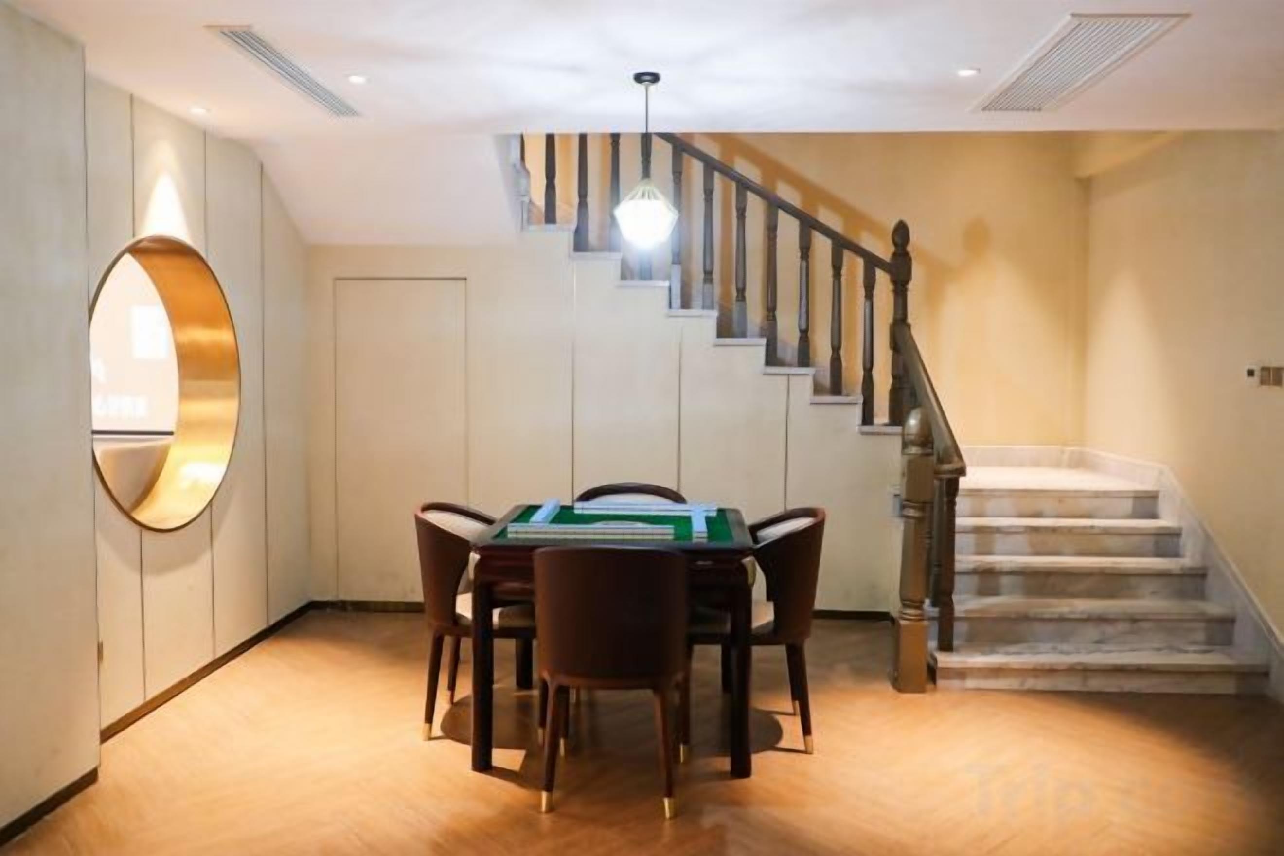 A dining area with a table and chairs, a staircase, and a circular mirror on the wall.