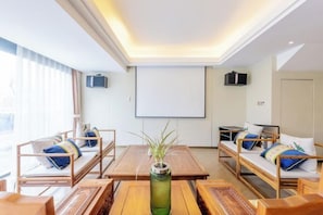 Habitación de hotel con una cama grande, dos mesitas de noche, una mesa de centro de madera y una pantalla para proyector.