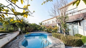 Una piscina con solárium de baldosas, rodeada de vegetación y un edificio al fondo.