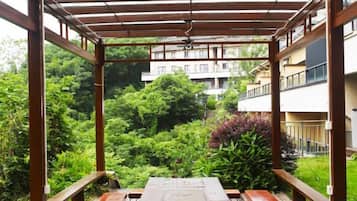 Un espacio al aire libre cubierto con un banco de madera, rodeado de abundante vegetación y vistas a un edificio residencial.