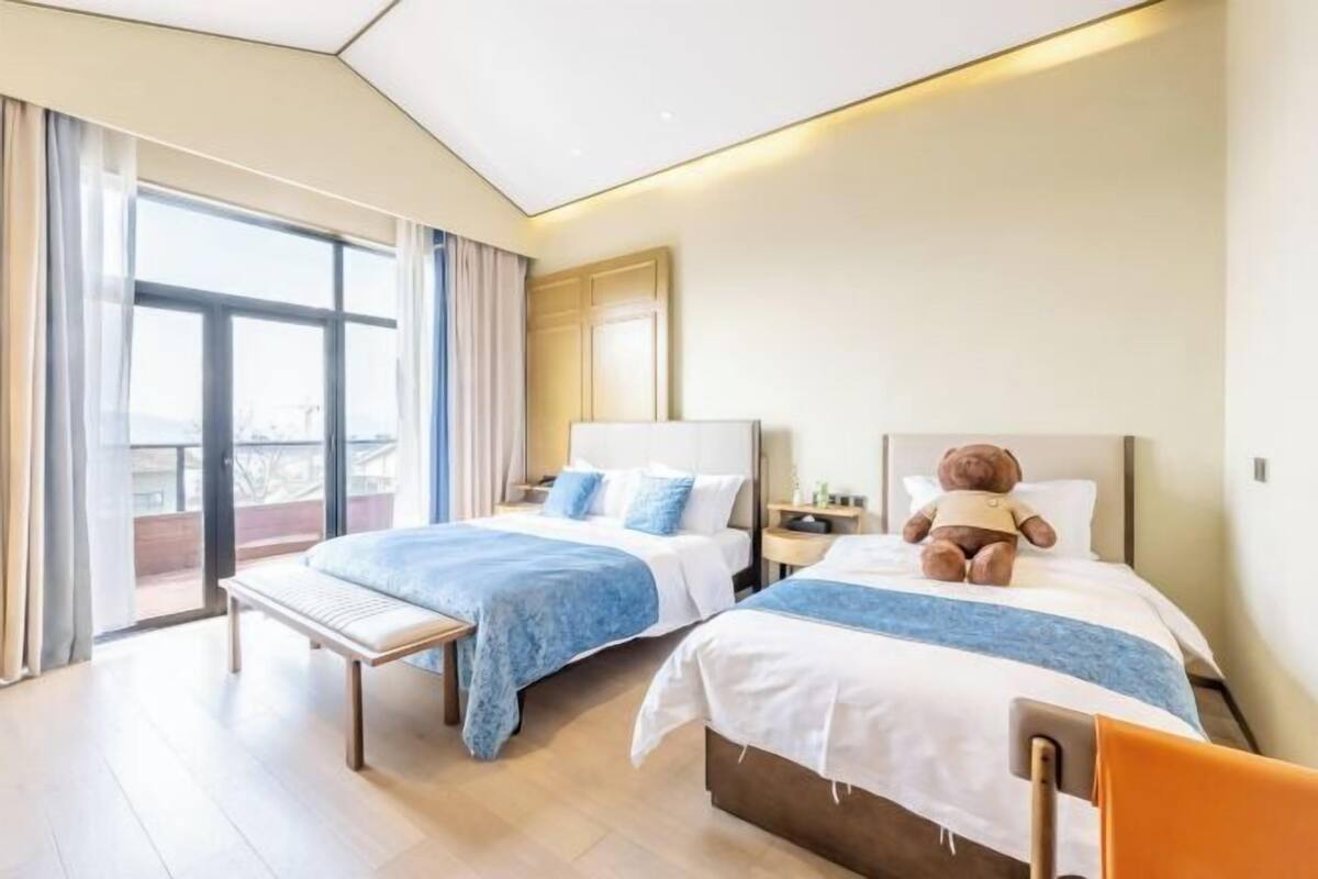 A hotel room with two beds, a bench, a large window, and a view of the city.