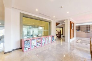 Un vestíbulo amplio con diseño moderno, que cuenta con un muro de vidrio, una hilera de máquinas expendedoras y una escalera que lleva a otra zona.