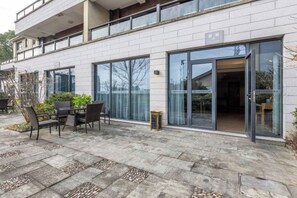Un edificio moderno con un patio que cuenta con una mesa, sillas, grandes puertas de cristal y un piso de baldosas de piedra.