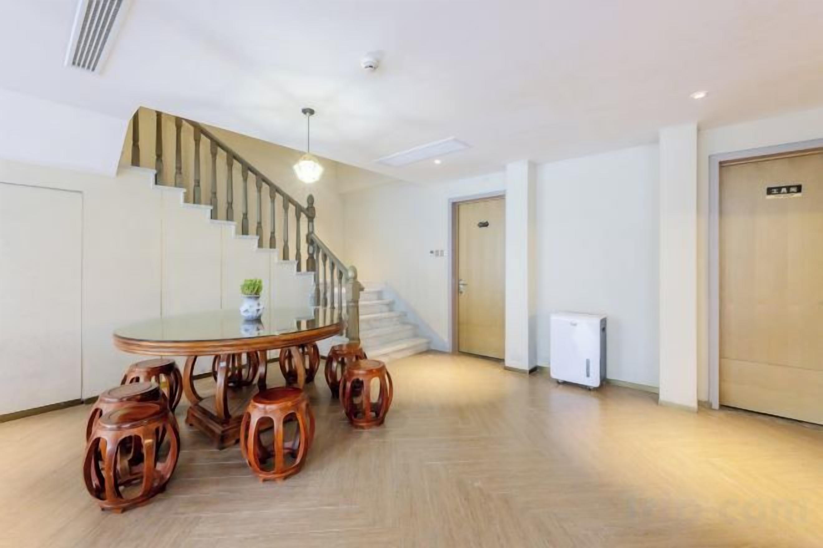 A hotel lobby with a round table, wooden stools, a staircase, and a door.