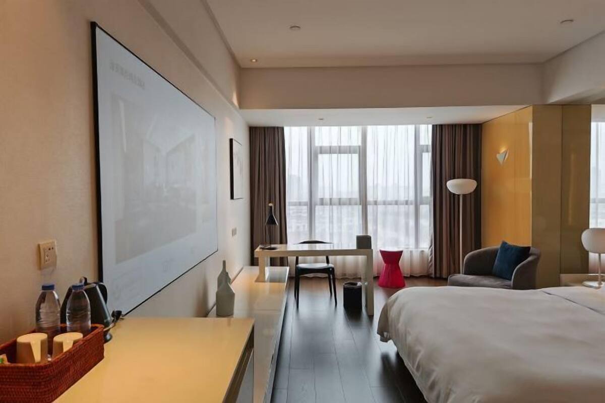 Una habitación de hotel con cama, escritorio, silla, televisor y ventana con cortinas.
