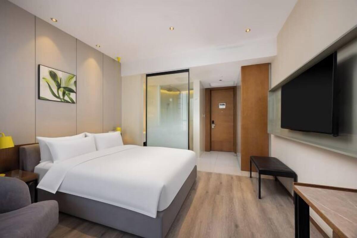 Una habitación de hotel moderna con cama, mesita de noche, televisión y una puerta corredera que da acceso a un baño.