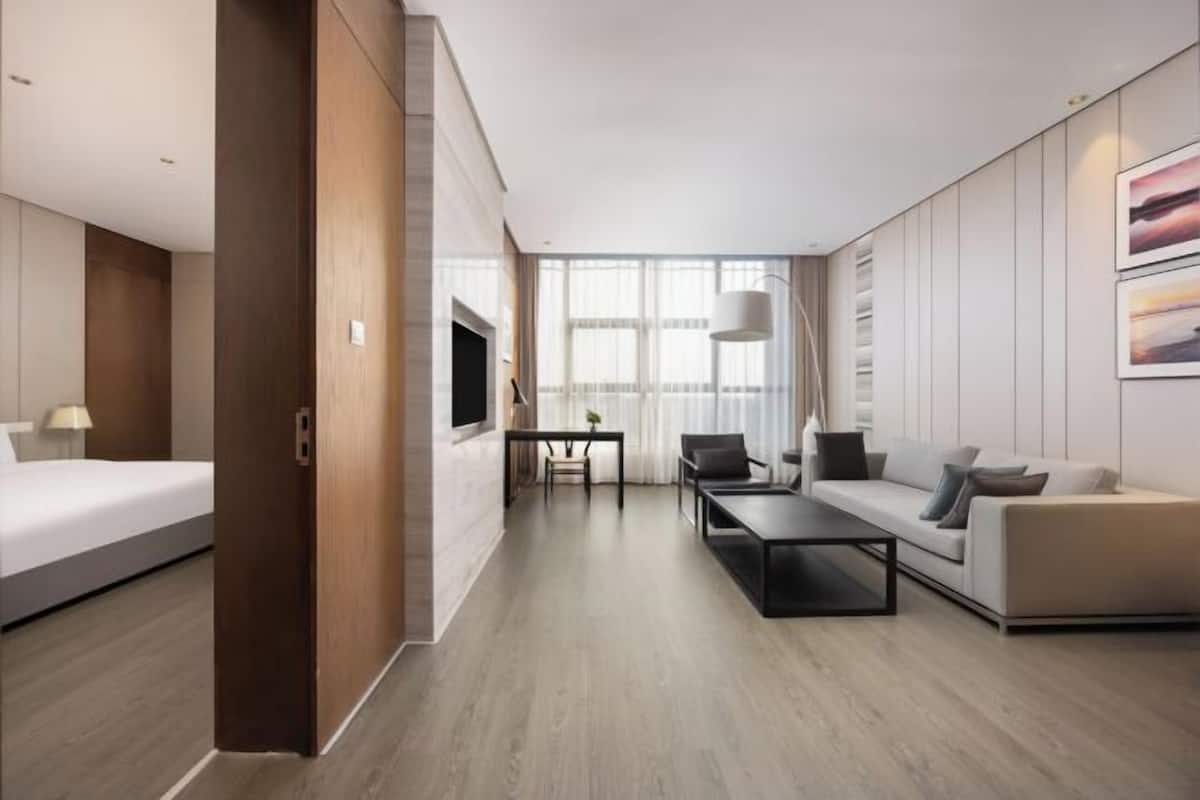 Una habitación de hotel moderna con cama, sofá, mesa de centro y televisión.
