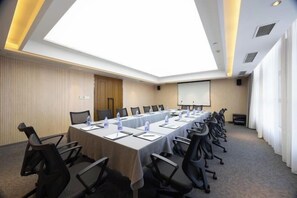 Une salle de conférence avec une longue table, des chaises, un écran de projection et une grande verrière.