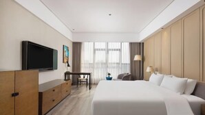 Une chambre d’hôtel avec un grand lit, une télévision, un bureau et une vue sur la ville grâce à de grandes fenêtres.