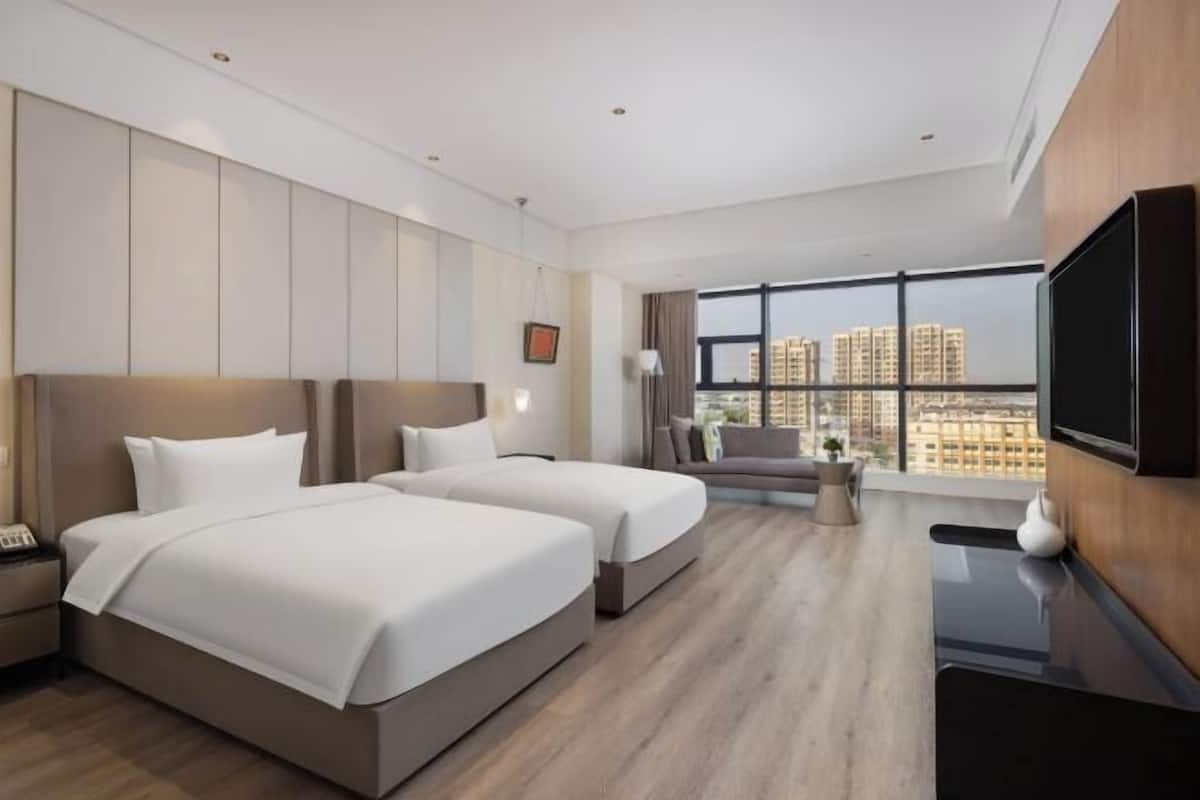Una habitación de hotel moderna con dos camas, un sofá, un televisor y un ventanal con vistas a la ciudad.
