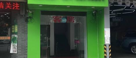A hotel entrance with a green facade, a visible phone number, and a sign indicating a room type.