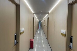 Un couloir d’hôtel avec des portes portant les numéros des chambres et une poubelle rouge.
