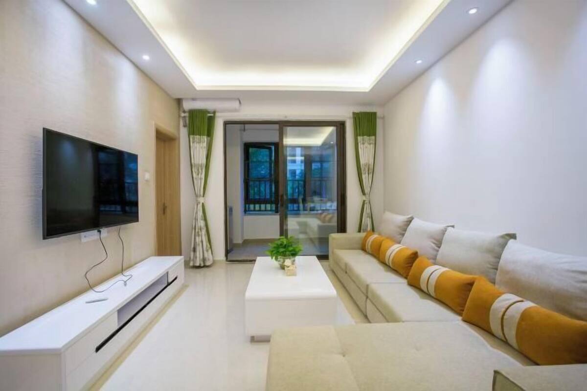 A modern living room with a flat-screen TV, a white coffee table, and a sofa with yellow cushions.