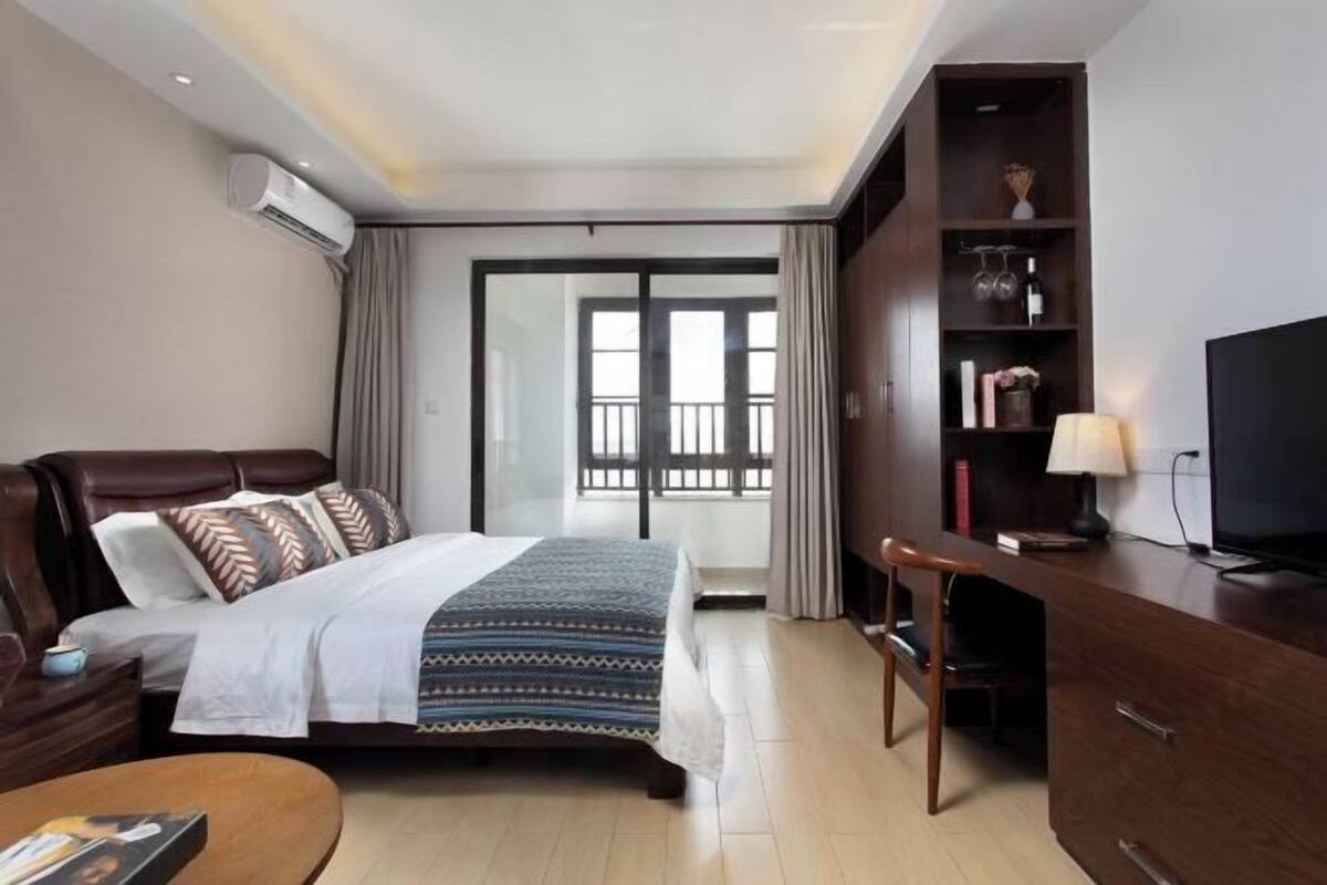 A hotel room with a bed, a desk, a chair, a TV, and a bookshelf.