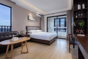 A hotel room with a bed, a sofa, a table, a bookshelf, and a large window.