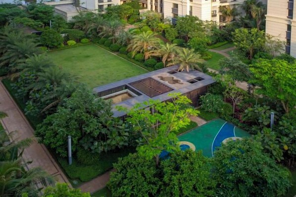 An aerial view of a hotel courtyard with a tennis court, lush greenery, and a pool area.