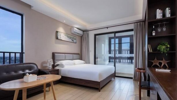 Una camera d'albergo con un letto, un tavolo in legno, una poltrona, una libreria e un balcone con vista.