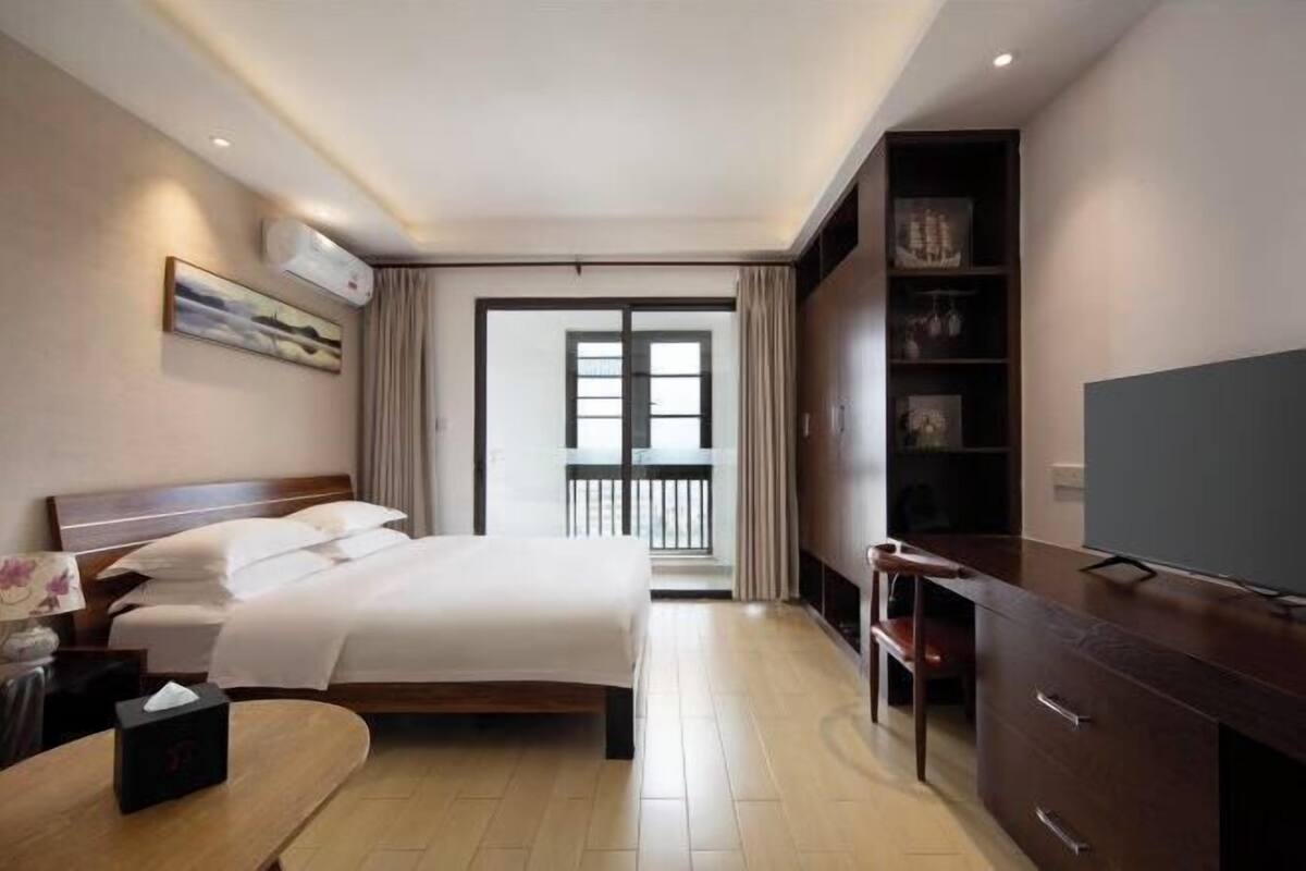 A hotel room with a bed, bedside table, TV, wardrobe, and a balcony view.