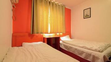 A room with two beds, a nightstand, a lamp, and a window with curtains.