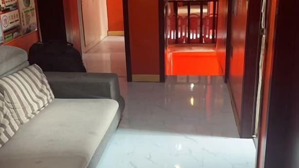 Quarto de hotel com sofá, mala e corredor que leva a uma área iluminada em vermelho.
