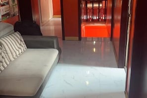A hotel room with a sofa, a suitcase, and a hallway leading to a red-lit area. - Jiye Hostel (Zhenjiang)