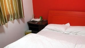 Uma cama de solteiro com roupa de cama branca num quarto com parede vermelha e cortina.
