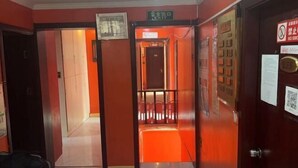 Corredor de hotel com parede vermelha, um elevador e uma porta com aviso de 'Não Fumar'.