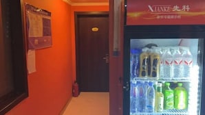 Corredor com geladeira abastecida de bebidas e porta com extintor de incêndio.