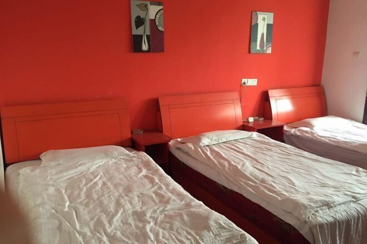A room with two single beds, each with a wooden headboard and white bedding. There are two nightstands with red surfaces, and the walls are painted red.